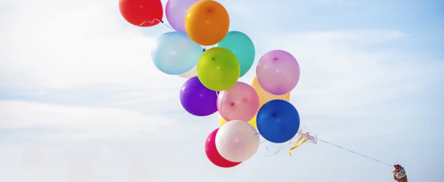 Dłoń trzymająca kolorowe balony, w tle widoczne niebo i morze.